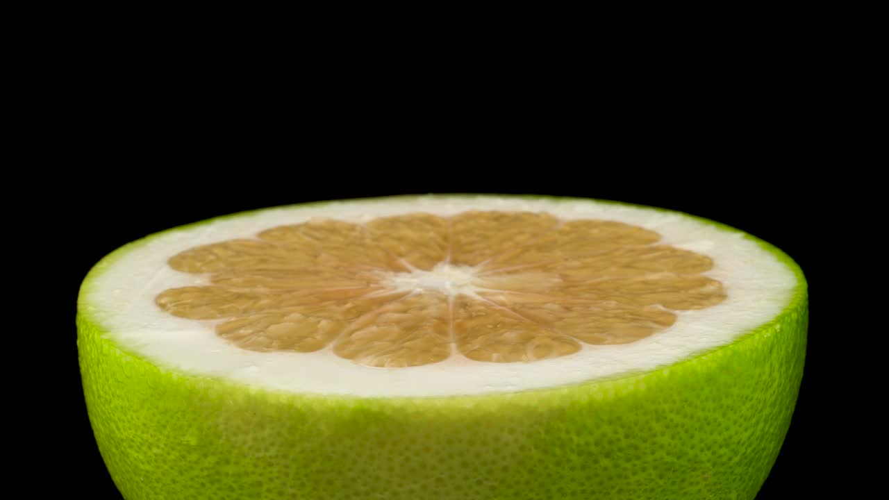 One half of green oroblanco fruit. Rotating on the turntable. Isolated on the black background. Close-up. Macro.