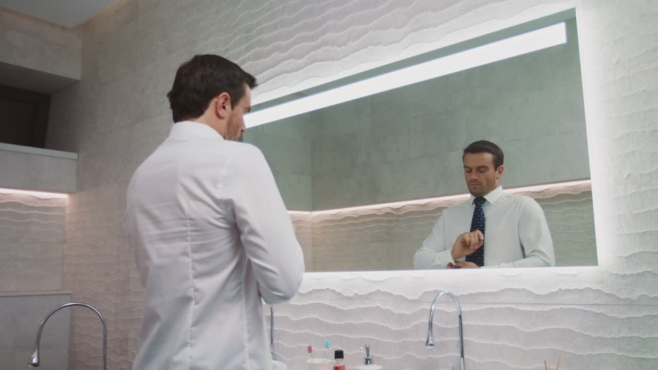 Uomo d'affari che si sistema la cravatta in un bagno di lusso. Uomo felice che indossa la cravatta in casa.