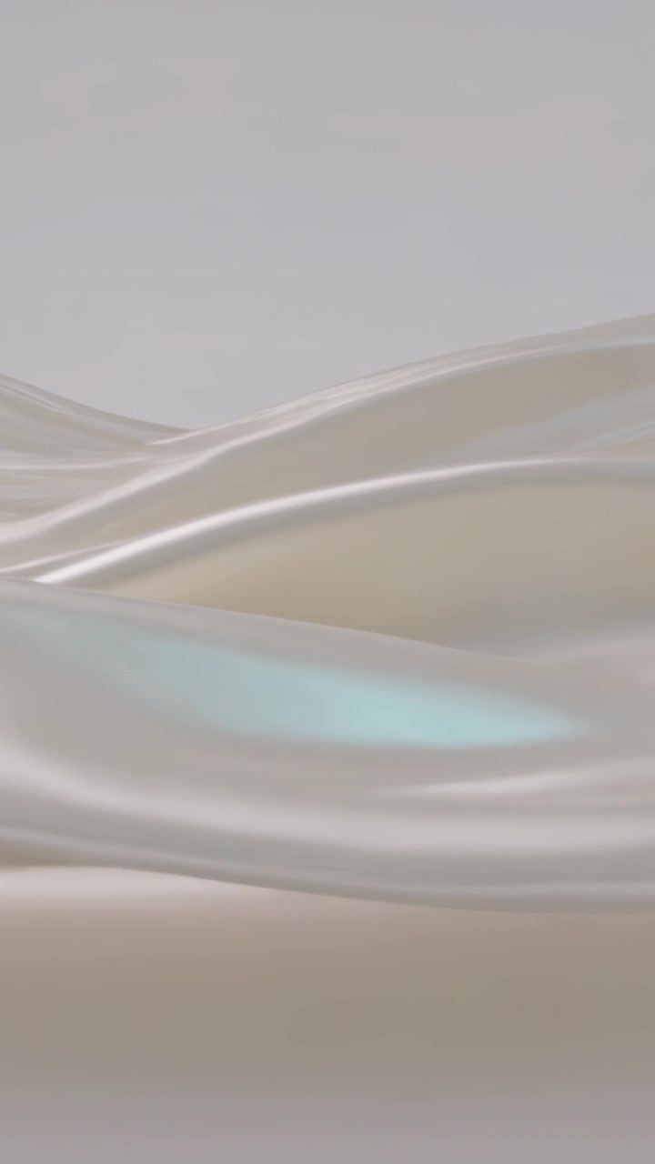 Vertical video: Rippling satin sheet drifting across gray backdrop as soft light highlighting sheen