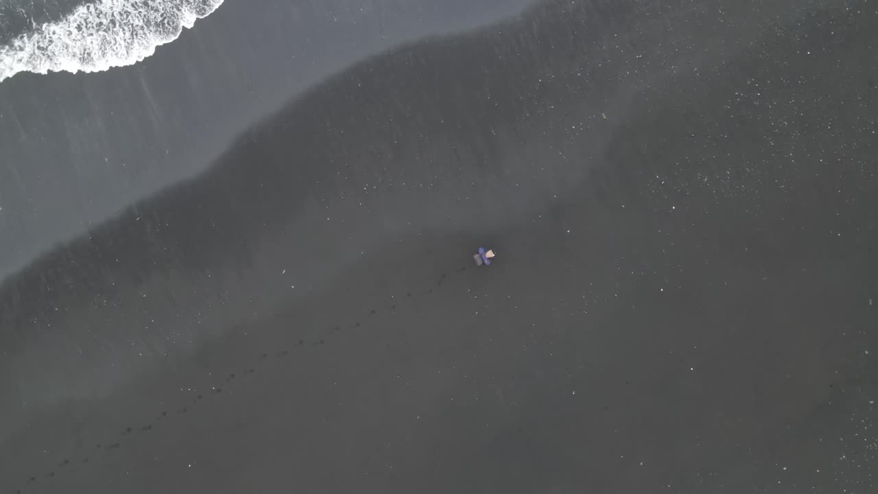 Person Walking on Black Sand Beach with Ocean Waves