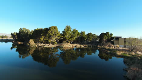 Fliegen-über-Eine-Teichoase-In-Der-Mojave-Wüste-Mit-Bäumen-Und-Himmel,-Die-Sich-Im-Wasser-Spiegeln