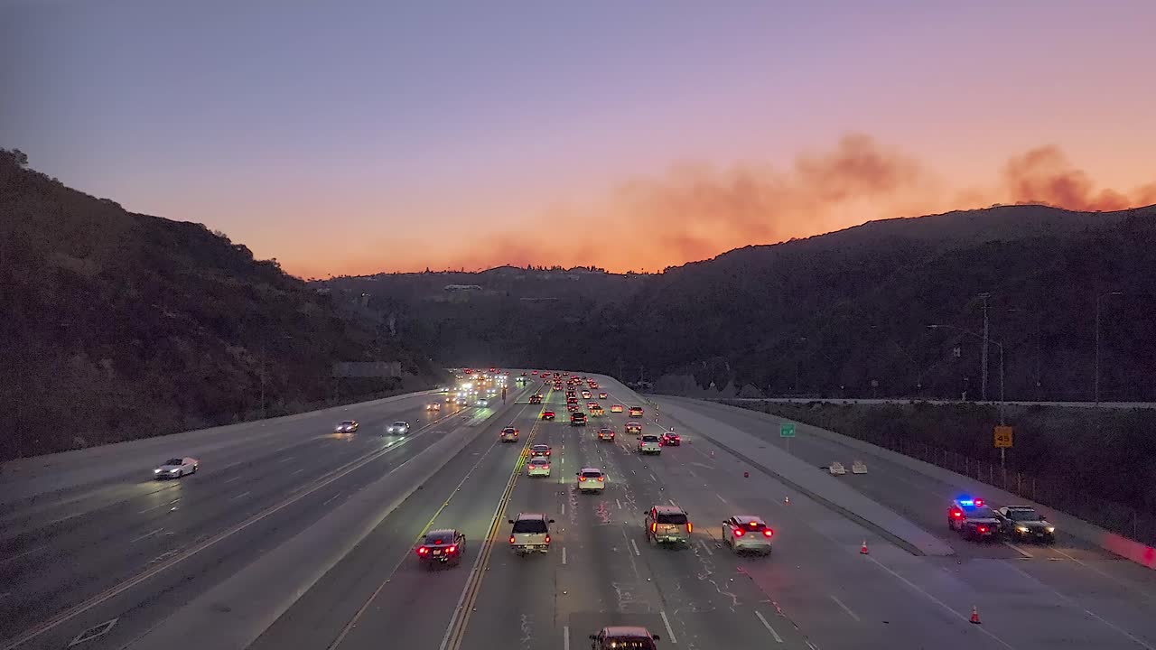 Cars driving on a highway with emergency vehicles and distant wildfires in California