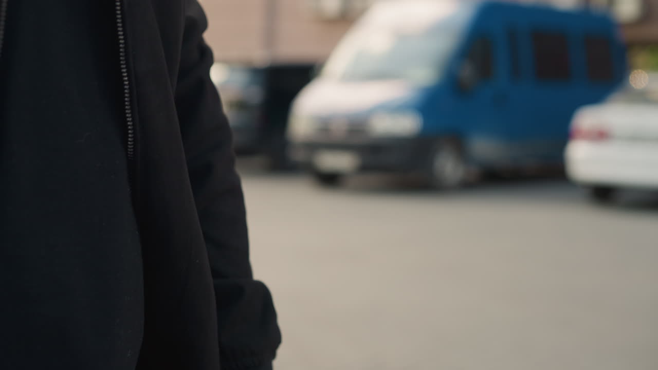 Asiatisk kurér justerer jakkeærmet udendørs nær varevogn, nærbillede af hænder på fortov, morgenlys, forbereder leveringsrute, fokuseret gestus, afslappet sort jakke, håndledsbevægelse, ærlig livsstil