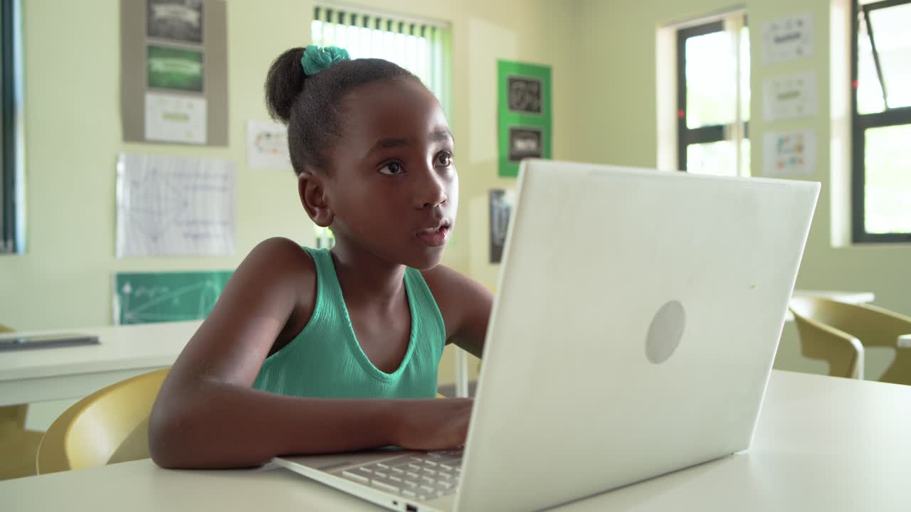 Compagni di classe con una ragazza afroamericana che scrive su un laptop in classe dopo aver svolto un compito, si ferma e sorride