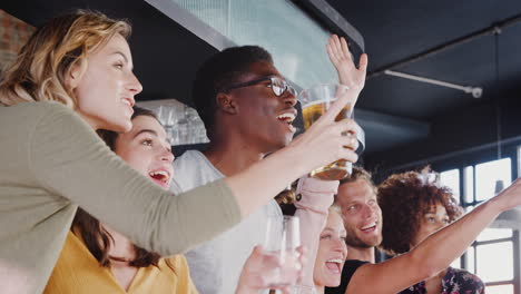 group of male and female friends celebrating whilst watching game on screen in sports bar