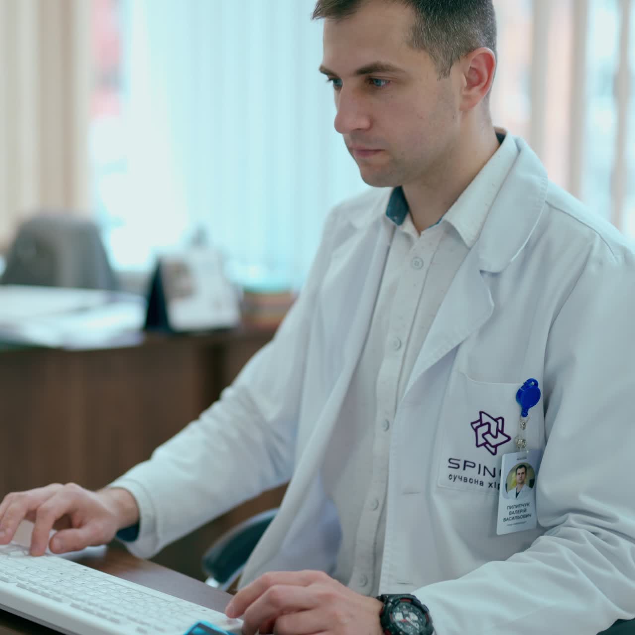 Young doctor sits at a table in cabinet. Male doctor in white coat working on his computer in medical office in clinic.