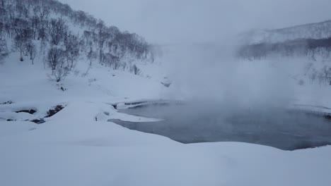 wide shot pan right of steam rising from hot spring in snow valley, niseko