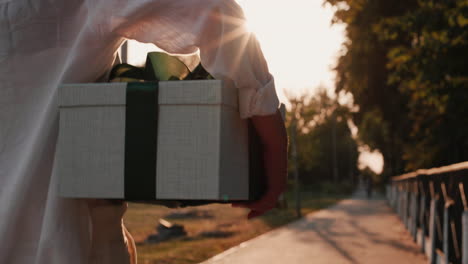 A-man-carries-a-beautifully-packed-box-with-a-gift-walks-down-the-street-in-the-sun