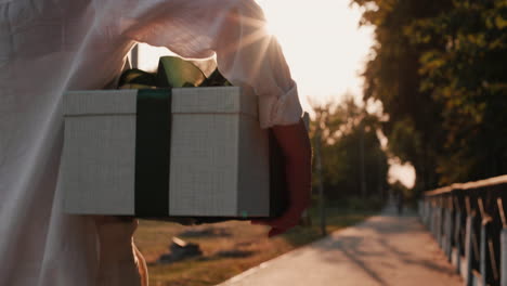 a man carries a beautifully packed box with a gift walks down the street in the sun