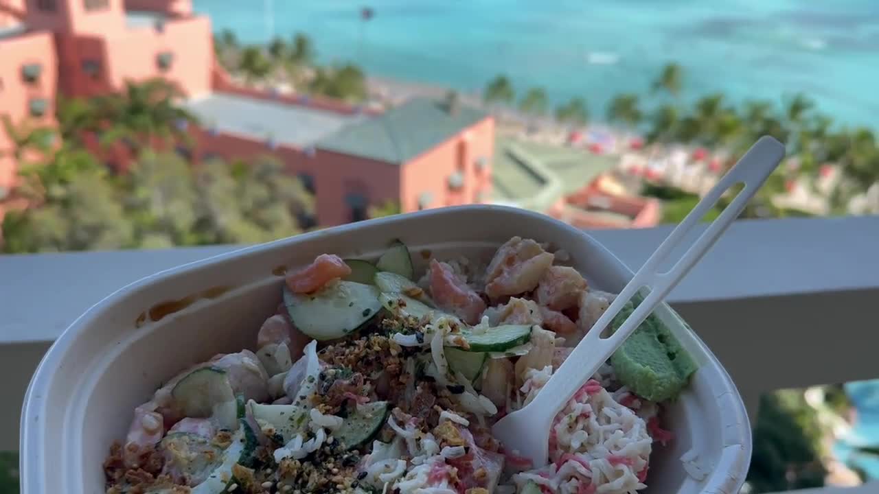 persona sosteniendo un delicioso tazón de poke hawaiano desde el balcón del hotel con vista a la playa de waikiki
