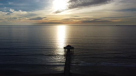 romantic flight to the horizon with sun and clouds over the silhouette of a roundhouse aquarium with a pier, under a calm and idyllic sunset, california