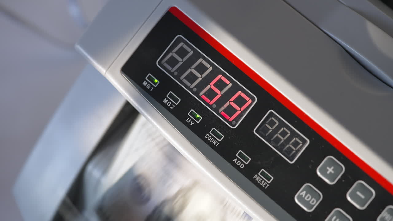 Numbers changing quickly on the panel of cash counting machine. Device at work, lamps are on. Close up.