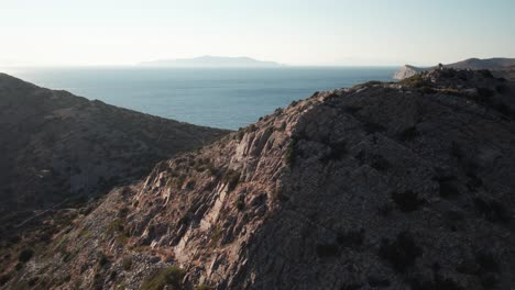 aerial dolly push in over shrub ridgeline and rocky outcropping above coastline in syros greece