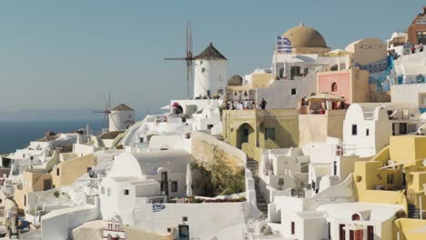 Cierre-Pan-Revelan-Molinos-De-Viento-Tradicionales-Blancos-Y-Bandera-Griega-En-Santorini,-Grecia