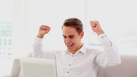 Cheering-attractive-man-using-his-laptop-sitting-on-couch