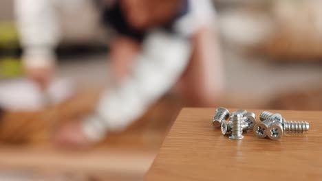 close-up of metal screws on a table with blurred background of furniture assembly in a well-lit room
