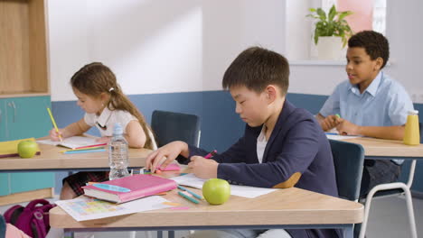 male student sitting at desk in english classroom writting in her notebook 1