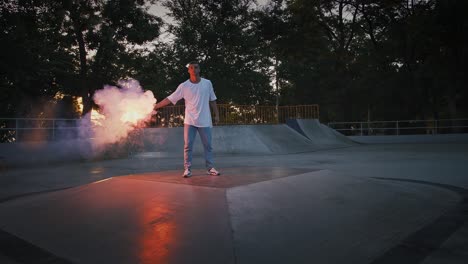 young man in casual clothes is holding glowing red signal flare and going to perform breakdance on pump track of skatepark. slow motion