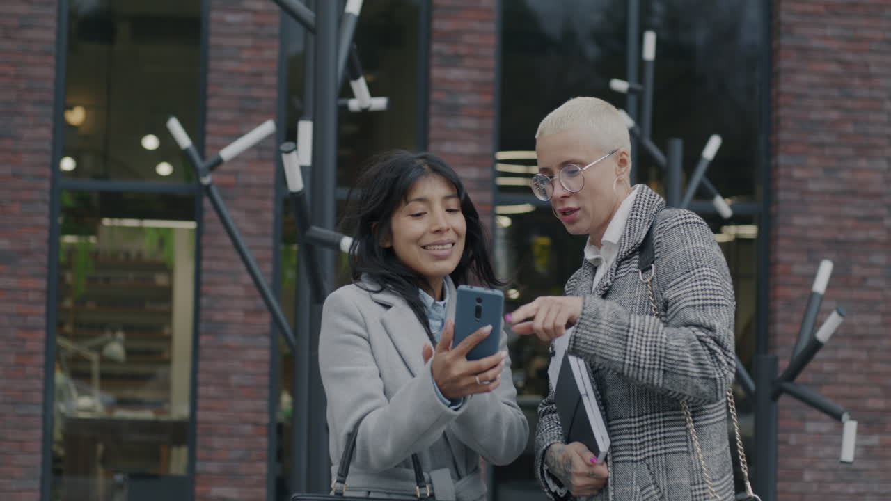 Donne d'affari che discutono sullo smartphone fuori da un edificio per uffici