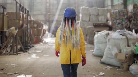 waste processing plant. recycling and storage of waste for further disposal. woman worker in hard hat walking through the stacks of pressed disposal waste, huge piles. rare view