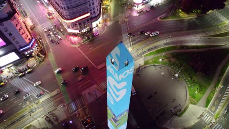 órbita-Aérea-Del-Obelisco-En-Buenos-Aires,-Con-Los-Colores-De-La-Bandera-Argentina,-Animando-Al-Equipo-Nacional-De-Fútbol-En-La-Copa-Del-Mundo-Qatar-2022,-Avenida-Corrientes-Y-Anuncios-De-Luces-De-Neón