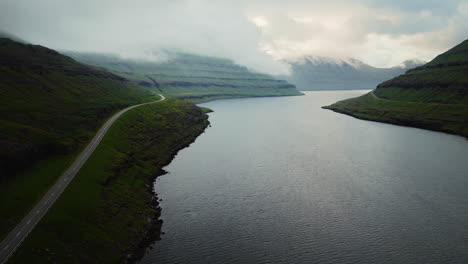 Scenic Fjord Landscape with Winding Road and Cloud-Covered Mountains