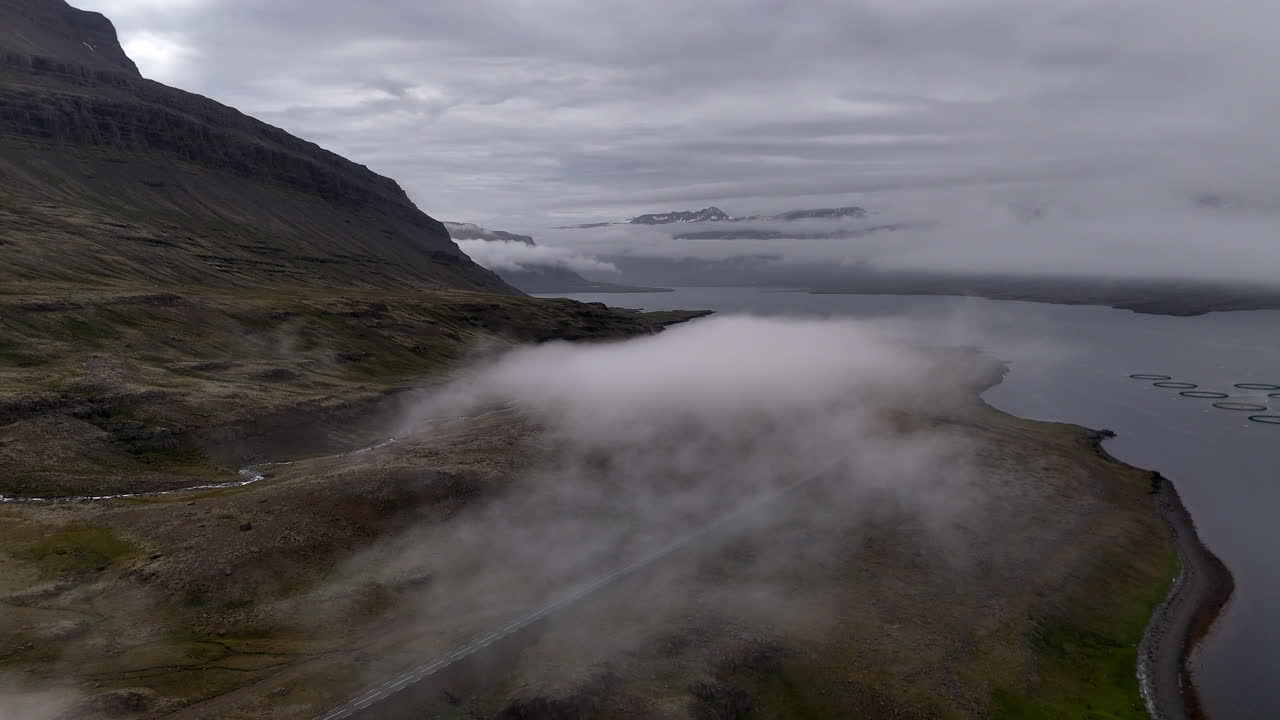Misty mountain slopes and small waterfalls overlook Berufjörður as drifting clouds slide across the rugged Icelandic landscape