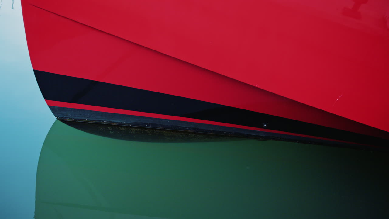 Close up of a red and black boat hull reflecting on calm turquoise water