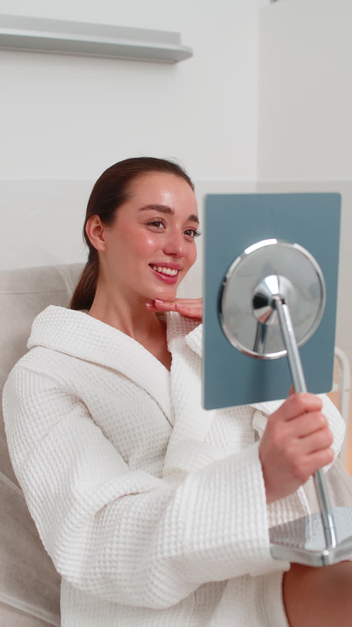 Caucasian young woman smiles in mirror after facial therapy in beauty clinic showing visible result