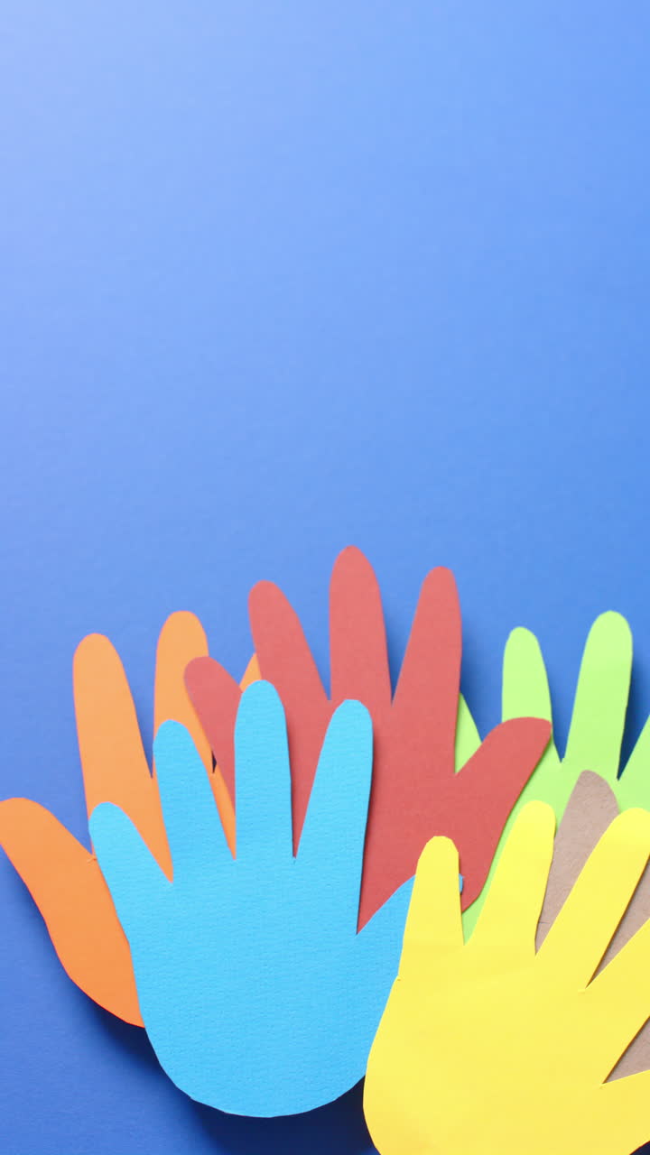 Vertical video of hands together made of colourful paper on blue background with copy space