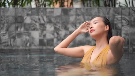 beautiful asian woman relaxing in swimming pool, fixing her wet hair, close up slow motion