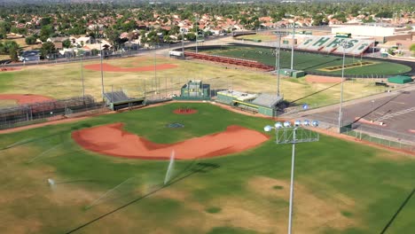 aerial arc around an empty baseball diamond where sprinklers water the outfield.