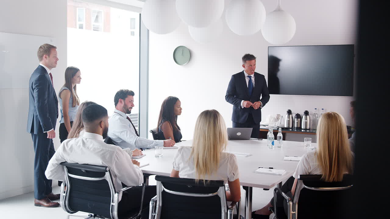 성숙 한 사업가 가 졸업생 채용 평가 날 에 테이블 주위 집회 를 연설 하고 있다
