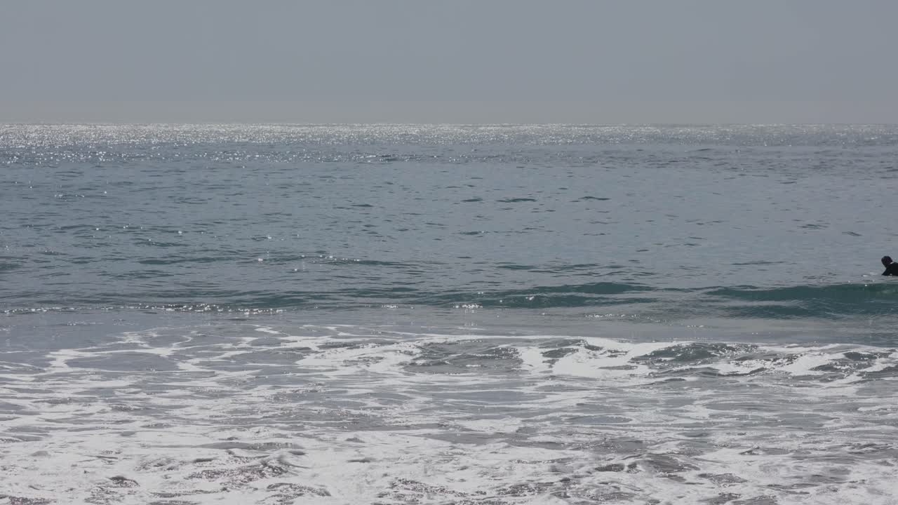 남자 서퍼는 일출 때 바다에서 작은 파도를 잡으려고 노를 젓는다