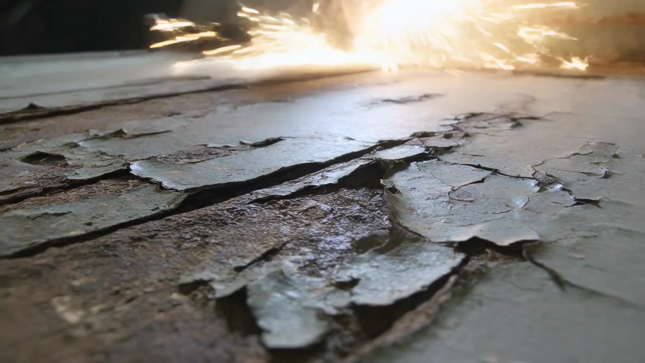 Scintille provenienti da una smerigliatrice fuori campo durante la lavorazione, che si riflettono su una superficie verniciata scrostata sul davanzale della finestra.