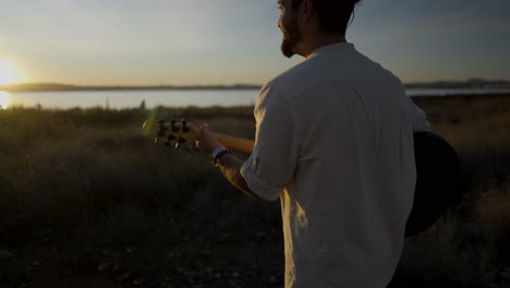 man playing guitar at sunset by the lake