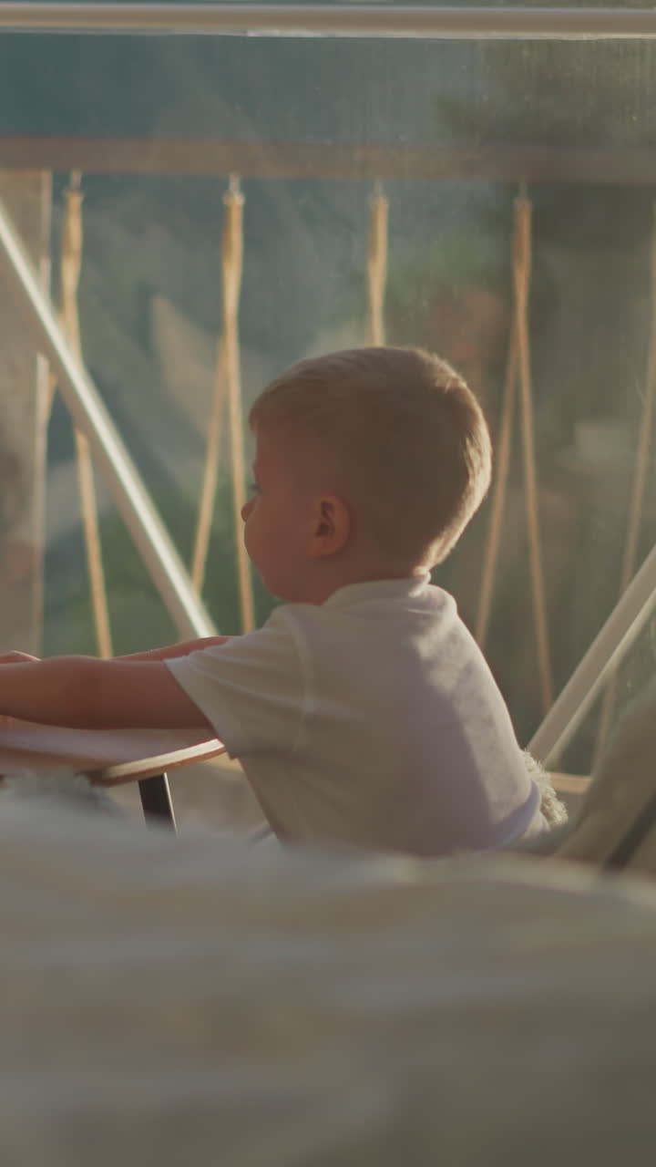 Siblings rests sitting at table in hotel. Boy pushes away empty cup at breakfast. Brother and sister look at landscape in transparent glamping tent
