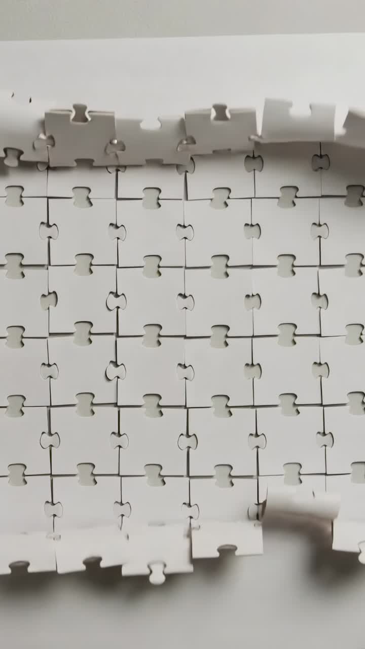 Video verticale: Partendo da una striscia, mani che posizionano tessere di puzzle ad incastro su un foglio, formando una griglia.