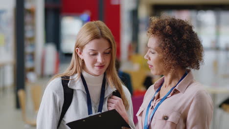 female college student meeting with woman tutor in busy communal campus building