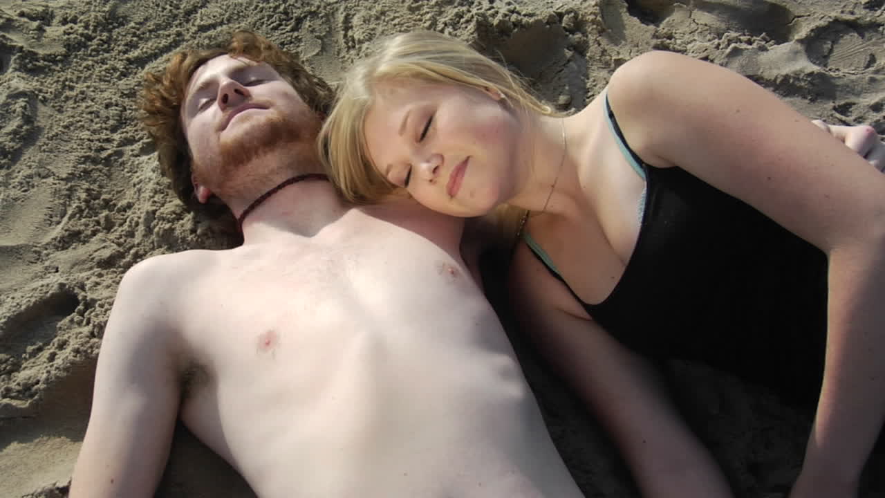 una mujer empaca arena en el pecho desnudo de un hombre y luego dibuja un corazón con el dedo mientras yacen en la playa