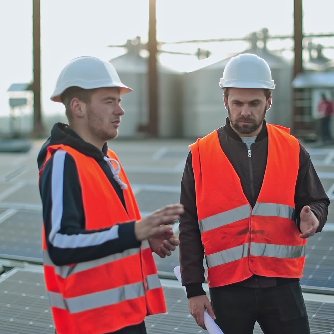 Technicians on photovoltaic farm of a renewable energy. Two workers in safety helmets are talking on the background of solar panels.