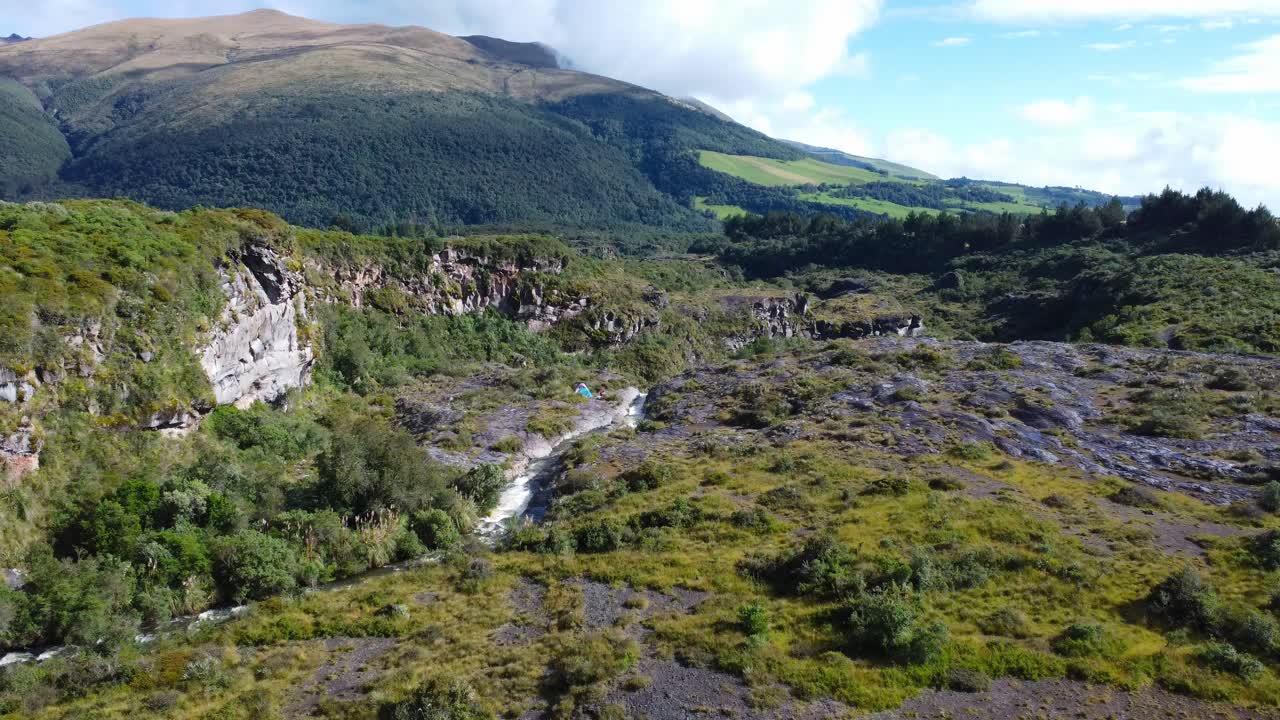 Aerial dolly-in and tilt-down shot capturing a river leading to Fuego Waterfall near Cotopaxi, Ecuador. As the camera moves forward, a hidden campsite beside the cascade is revealed.