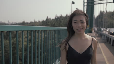 medium shot of beautiful smiling asian woman walking on lions gate bridge in vancouver, slowmo