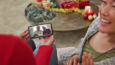 Smiling-asian-couple-using-smartphone-for-christmas-video-call-with-happy-family-on-screen