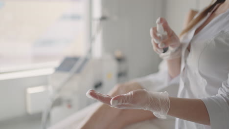 cosmetólogo o médico terapeuta mujer rociando desinfectante en las manos con guantes antes del tratamiento médico