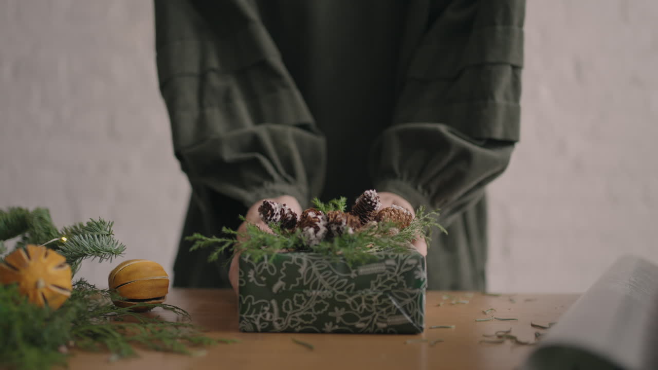 A Christmas present moves a woman's hands into the camera. Green Packaged Gift Woman Moves Into Camera After Packing and Decorating