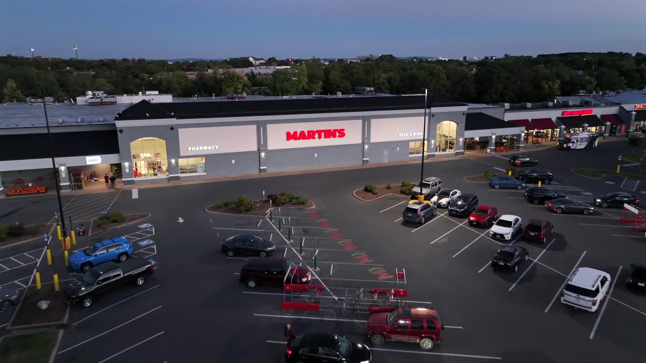 Parking cars in front of american Shopping mall at dusk. Pharmacy and Martins Storefront in Virginia. Aerial approaching shot.