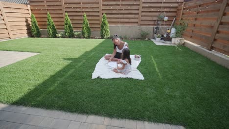 a mother and her young daughter sit on a blanket in the backyard, engaging in a drawing activity together. the outdoor scene captures a peaceful family moment, fostering creativity and bonding.