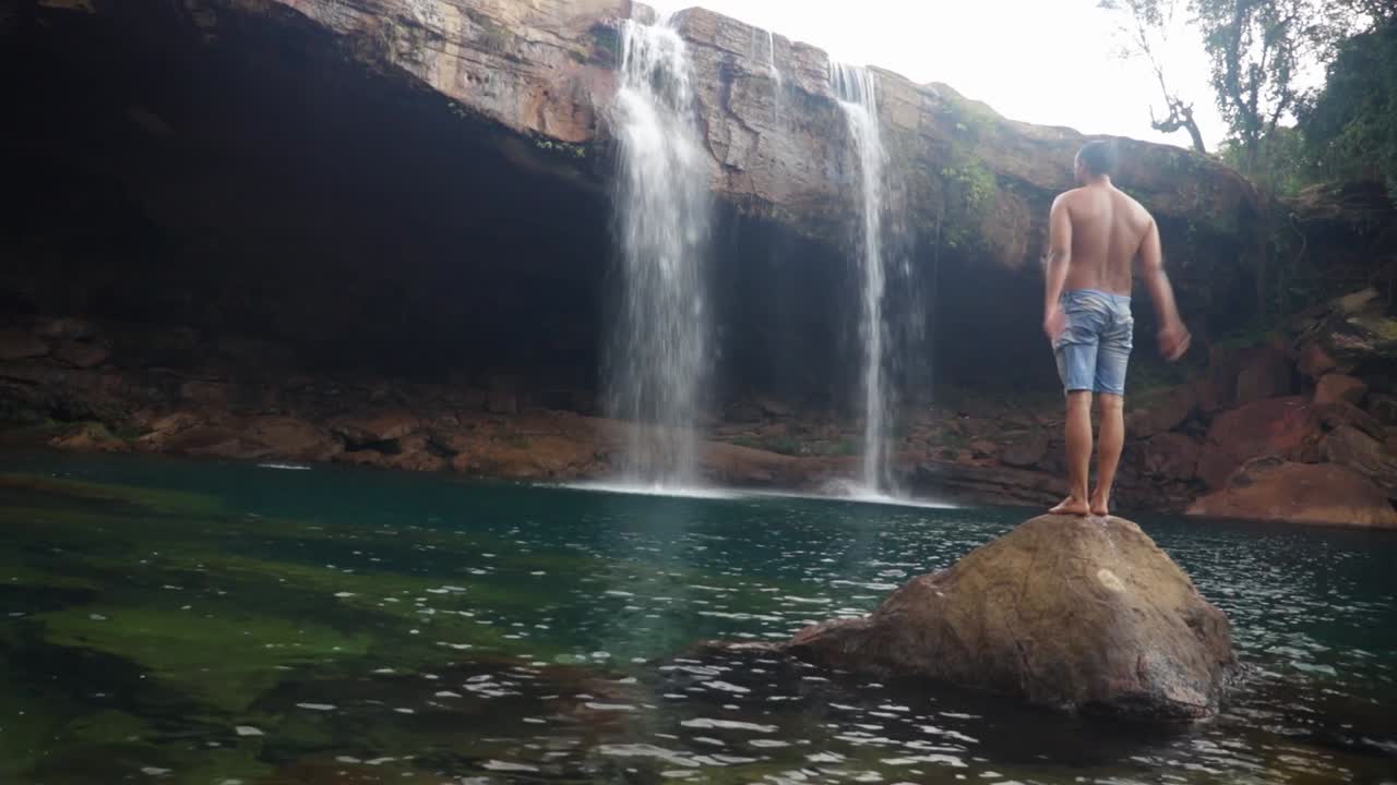 joven saltando en la cascada natural que cae desde la cima de la montaña en el video matutino tomado en la cascada krangsuri meghalaya india
