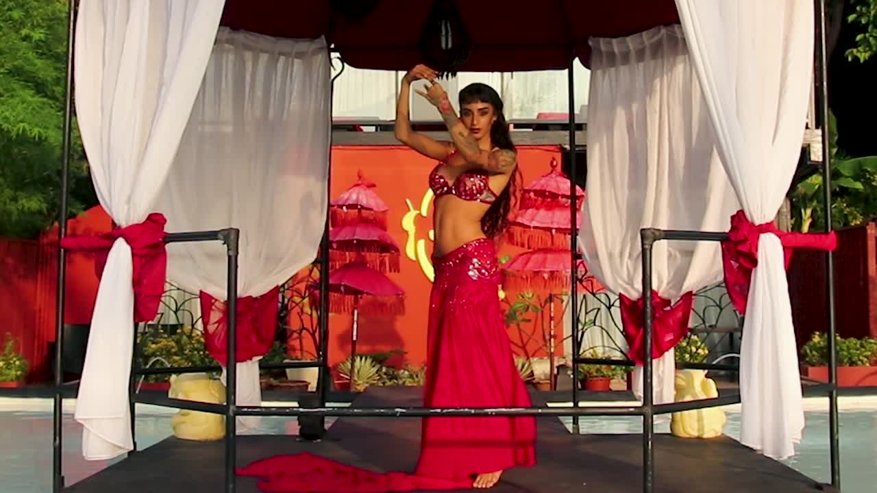 Elegant, young and sexy belly dancer in red dress, performing under an Arabian gazebo at the resort